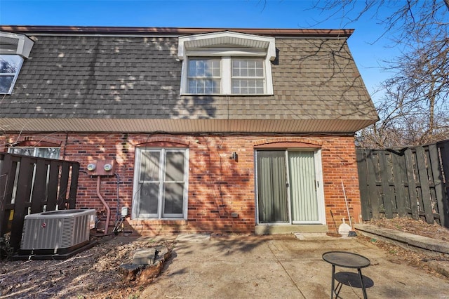 rear view of property featuring brick siding, fence, central AC, mansard roof, and a patio area