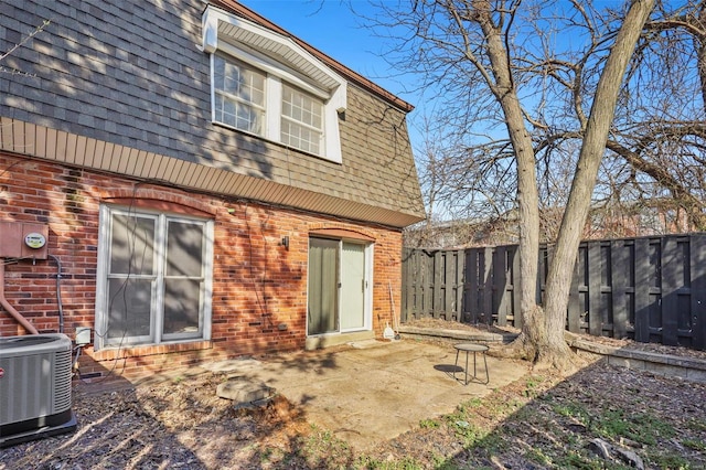 back of house featuring brick siding, roof with shingles, central AC unit, mansard roof, and a patio