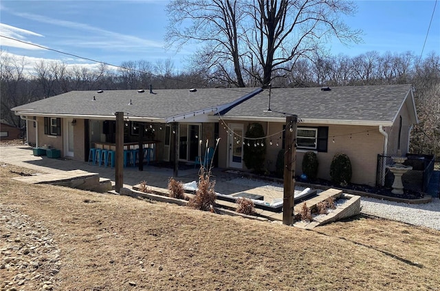 back of property with a patio area, roof with shingles, an outdoor bar, and brick siding