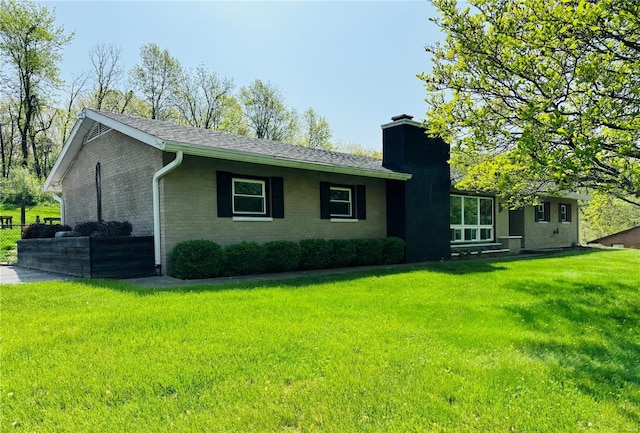 exterior space with a lawn, brick siding, a chimney, and a shingled roof
