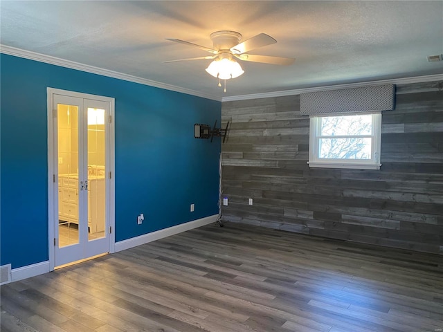 unfurnished room with ceiling fan, wood walls, baseboards, wood finished floors, and ornamental molding