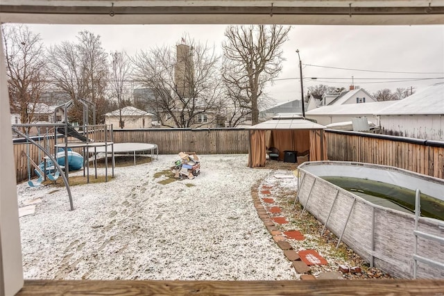 yard covered in snow featuring a gazebo, a playground, and a trampoline