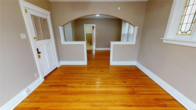 spare room featuring arched walkways, light wood finished floors, and baseboards