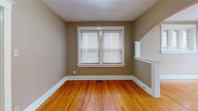 spare room featuring visible vents, baseboards, arched walkways, and wood finished floors