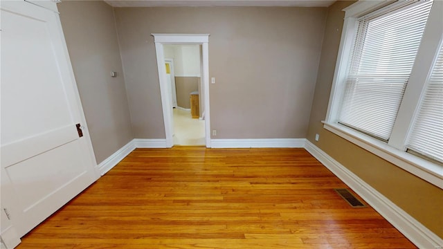 spare room featuring light wood-type flooring, visible vents, and baseboards