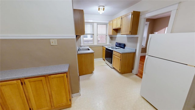 kitchen featuring a sink, light countertops, freestanding refrigerator, light floors, and range with gas cooktop