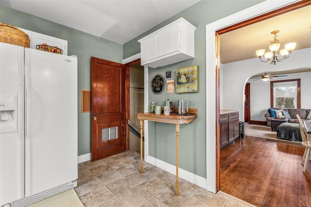 kitchen with white cabinetry, white refrigerator with ice dispenser, ceiling fan with notable chandelier, and light hardwood / wood-style floors