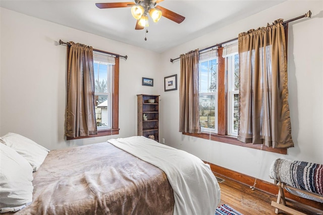 bedroom with multiple windows, wood-type flooring, and ceiling fan