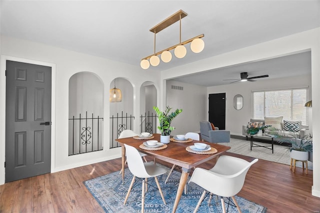 dining space featuring arched walkways, wood finished floors, visible vents, baseboards, and a ceiling fan