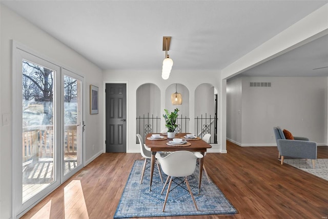 dining area with baseboards, visible vents, arched walkways, and wood finished floors