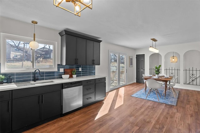 kitchen featuring arched walkways, light countertops, a sink, wood finished floors, and dishwasher