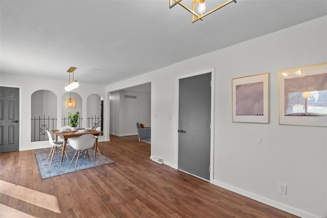 dining room featuring arched walkways, wood finished floors, visible vents, and baseboards