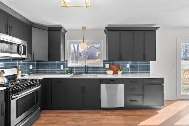 kitchen with a sink, light wood-style floors, light countertops, appliances with stainless steel finishes, and decorative backsplash