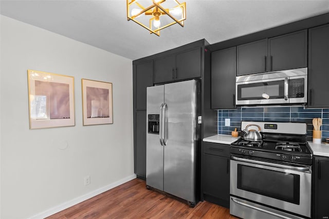 kitchen with stainless steel appliances, tasteful backsplash, light countertops, dark wood-type flooring, and dark cabinetry