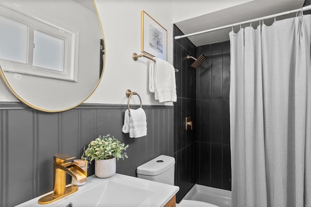 bathroom with a wainscoted wall, vanity, a tile shower, and toilet