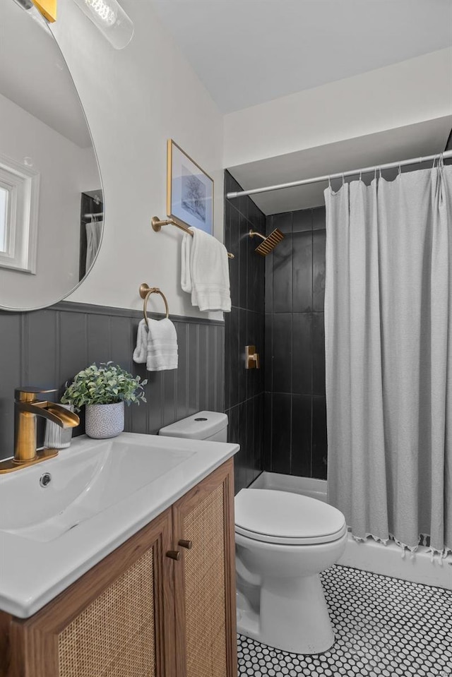 full bath with toilet, a wainscoted wall, tile patterned flooring, a tile shower, and vanity