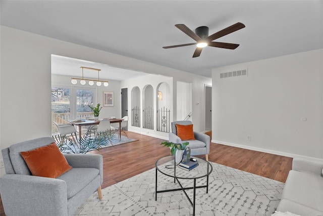 living room featuring visible vents, ceiling fan, baseboards, and wood finished floors