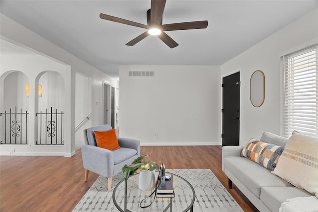 living area with baseboards, visible vents, arched walkways, ceiling fan, and wood finished floors