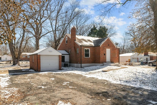 view of snow covered exterior with an outbuilding, brick siding, a chimney, and a garage