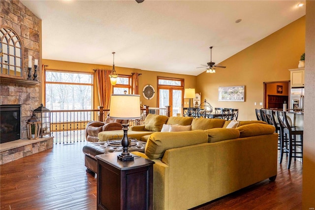 living room featuring ceiling fan, a stone fireplace, dark wood-type flooring, and high vaulted ceiling