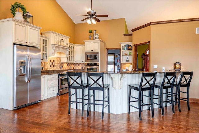 kitchen with dark hardwood / wood-style floors, a breakfast bar area, dark stone counters, kitchen peninsula, and stainless steel appliances