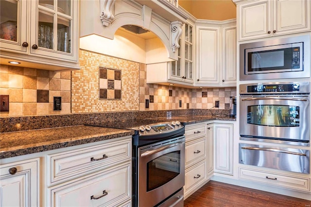 kitchen with stainless steel appliances, dark wood-type flooring, dark stone countertops, and decorative backsplash