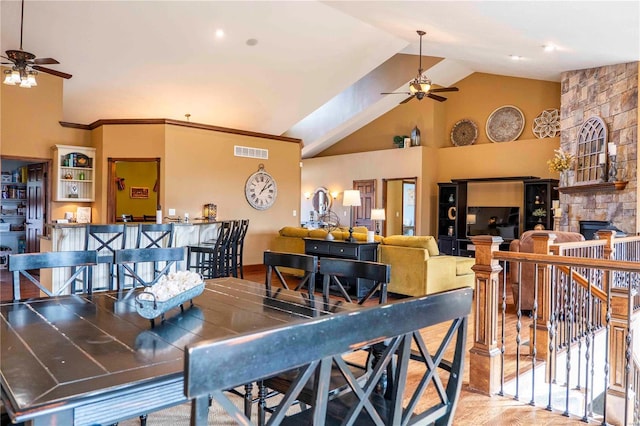 dining space with ceiling fan, ornamental molding, a fireplace, and high vaulted ceiling