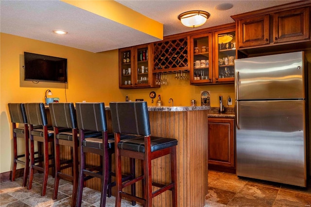 bar featuring light stone countertops, stainless steel refrigerator, and a textured ceiling