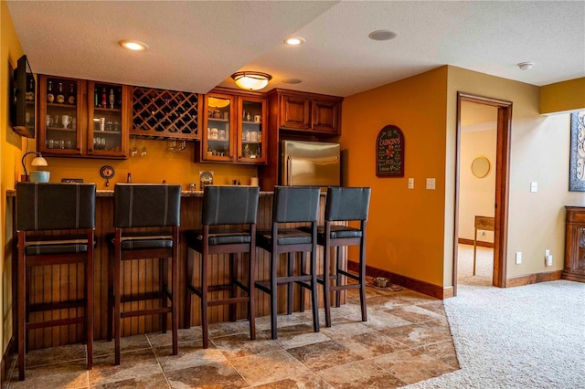 kitchen featuring a breakfast bar, stainless steel fridge, a textured ceiling, and carpet flooring