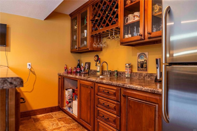 bar with dark stone counters, stainless steel fridge, and sink