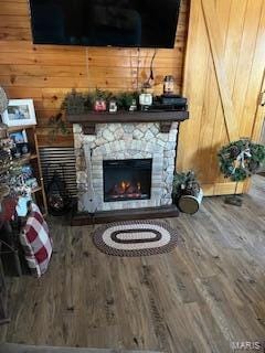 living room featuring wooden walls, a stone fireplace, and hardwood / wood-style floors