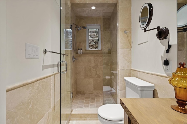 bathroom with toilet, vanity, tile walls, wainscoting, and a stall shower