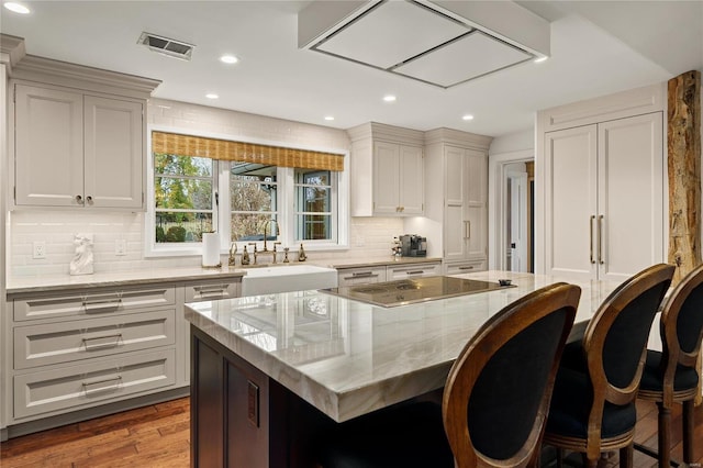 kitchen with wood finished floors, a center island, light stone countertops, black electric stovetop, and a sink