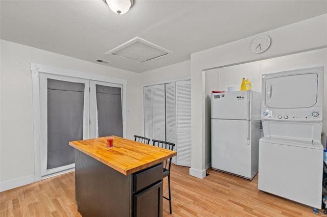 kitchen featuring stacked washer and clothes dryer, a breakfast bar area, a center island, light wood-type flooring, and white fridge