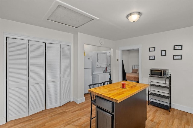 kitchen with a kitchen island, stacked washer / dryer, a kitchen breakfast bar, white fridge, and light hardwood / wood-style floors