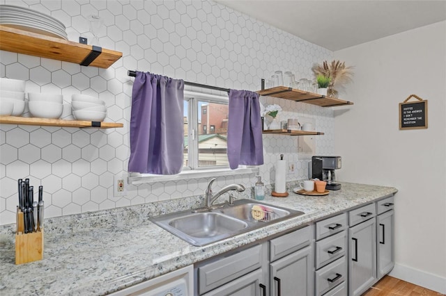 kitchen with tasteful backsplash, sink, light stone counters, and light hardwood / wood-style floors