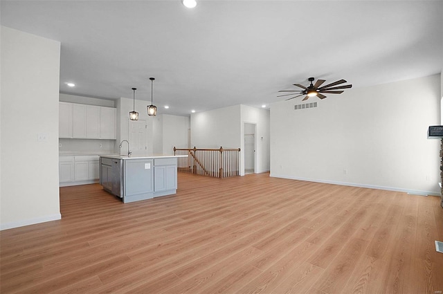 kitchen featuring sink, hanging light fixtures, light wood-type flooring, an island with sink, and white cabinets