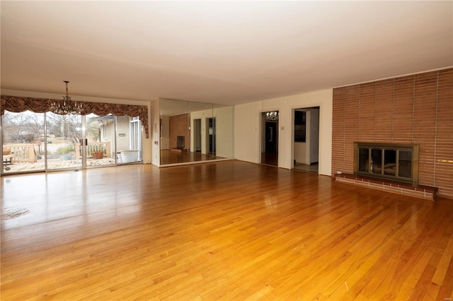 unfurnished living room featuring a brick fireplace, a notable chandelier, and light wood-style floors