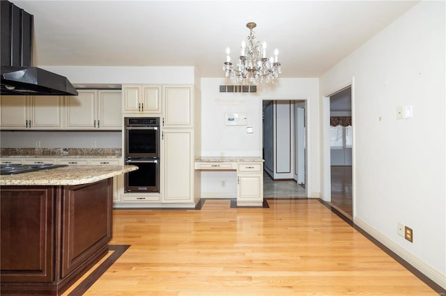 kitchen featuring black stovetop, visible vents, cream cabinets, double oven, and wall chimney range hood