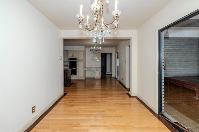 hallway featuring a chandelier, light wood-style floors, and baseboards