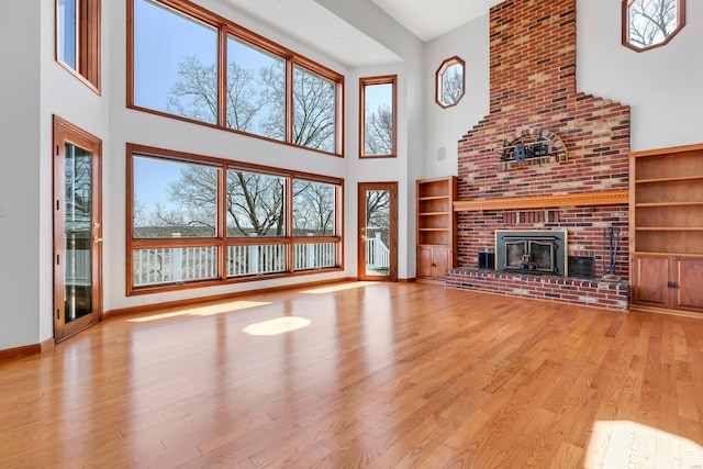 unfurnished living room with a fireplace, a high ceiling, baseboards, and wood finished floors