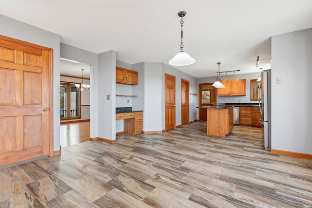 kitchen featuring baseboards, a kitchen island, built in study area, stainless steel appliances, and dark countertops