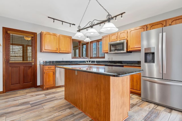 kitchen with a sink, stainless steel appliances, decorative light fixtures, light wood-type flooring, and a center island