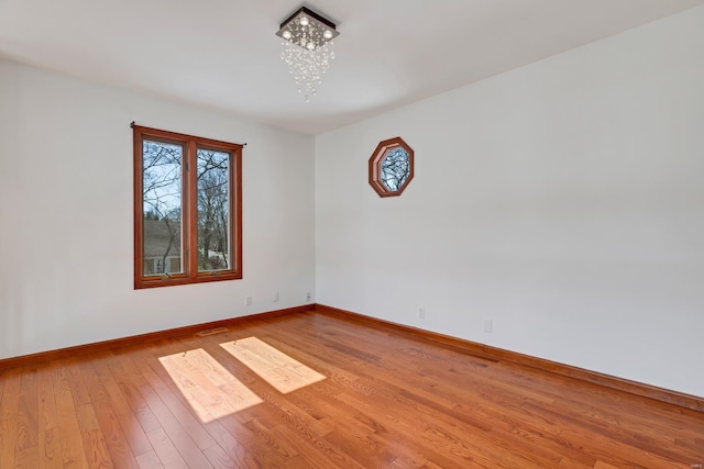 spare room featuring visible vents, baseboards, a chandelier, and light wood finished floors