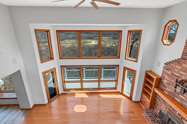 living room featuring baseboards, light wood-style floors, a high ceiling, and a ceiling fan