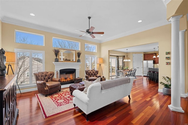 living room featuring crown molding, a glass covered fireplace, dark wood-style flooring, and decorative columns