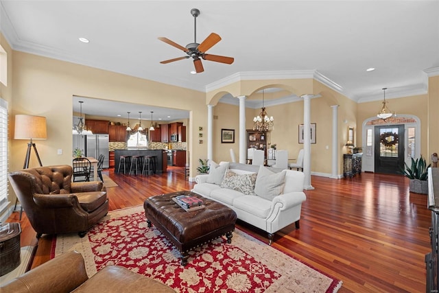 living room featuring arched walkways, wood finished floors, baseboards, ornate columns, and crown molding