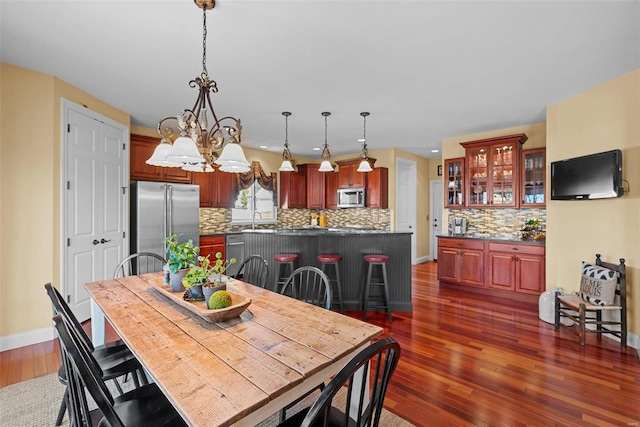 dining area with dark wood-type flooring, a notable chandelier, and baseboards