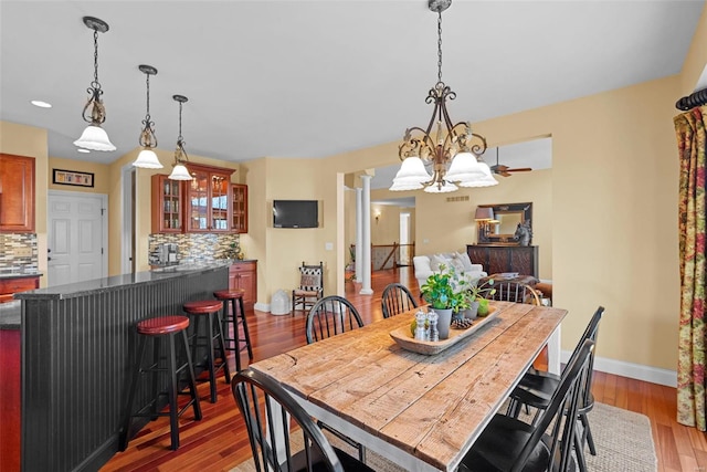 dining room featuring indoor bar, wood finished floors, baseboards, decorative columns, and an inviting chandelier