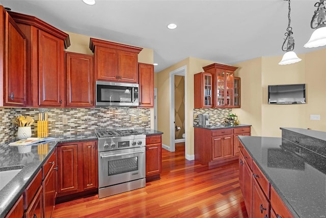 kitchen with appliances with stainless steel finishes, glass insert cabinets, decorative light fixtures, light wood-type flooring, and backsplash